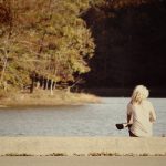 Woman sitting alone on a dock by a lake.