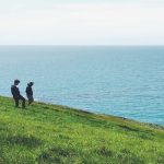 Two teenagers walking on a grassy hill by the sea