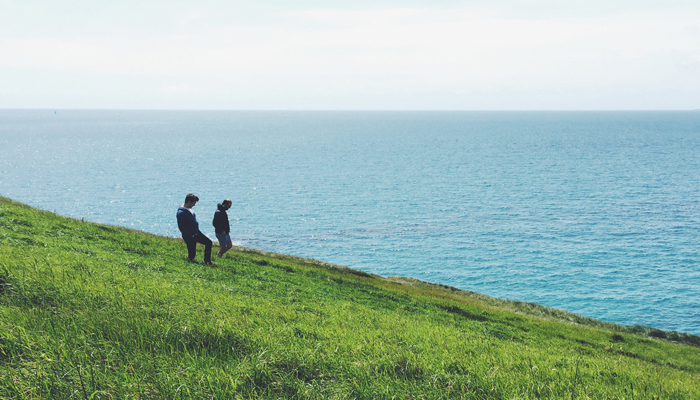 Two teenagers walking on a grassy hill by the sea
