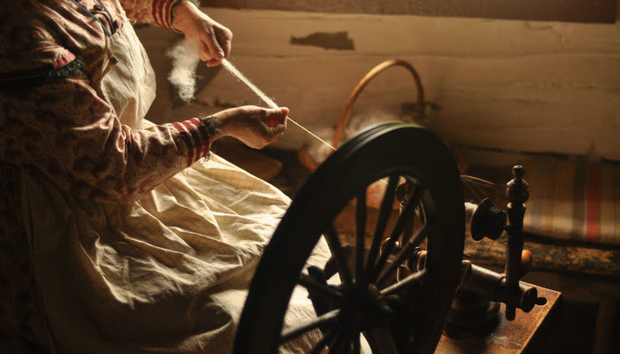 A pioneer woman spins thread using an old fashioned machine