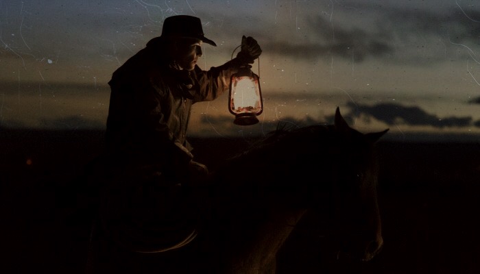 Cowboy riding a horse, holding a lantern.