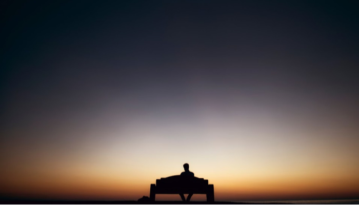 Silhouette of man sitting on bench.