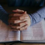man's praying hands on scriptures