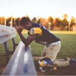 young man football player praying on sideline